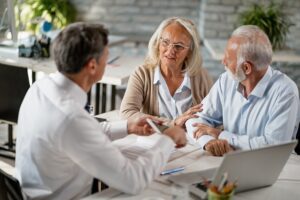 Senior couple communicating with insurance agent while having consultations with him in the office. Focus is on woman. Retirement: Discover if an employee's contract automatically end at legal age? Payroll Belgium